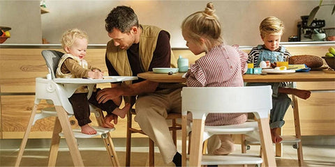 Un padre y sus hijos comparten la mesa con tronas evolutivas Stokke Steps blancas y naturales