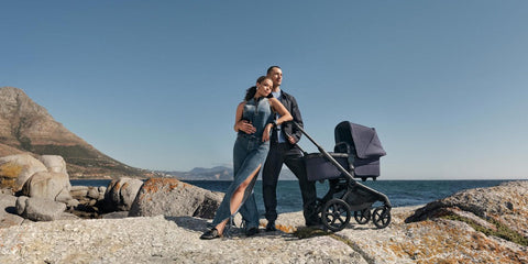 Una pareja junto a un Bugaboo Fox 5 Renew Deep Indigo con capazo en un paisaje costero