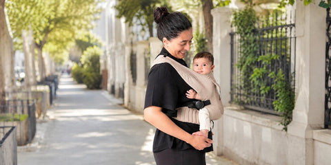 Mujer porteando a su bebé con una mochila Flybaby en un entorno urbano
